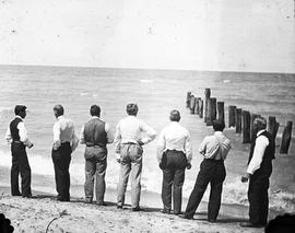 Beach event -- Men starring at water and pilings